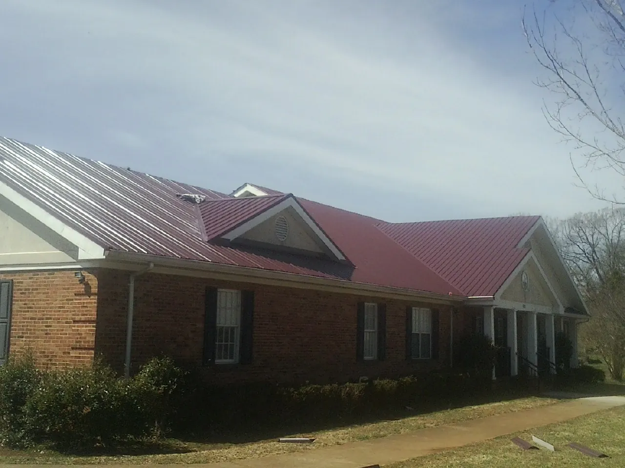 Red metal roof with gabled entries on a long brick building, from a Hail Damage Roof Repair job in Bennington