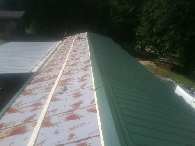 Old rusted panels beside newly installed green metal roofing — Wind Damage Roof Repair by Roofing Brothers in Bennington