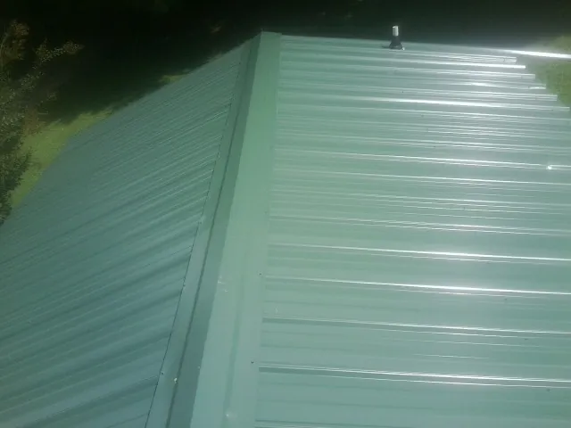 New green metal panels meeting at the ridge of a roof — Flat Roof Repair work by our crew in Bennington