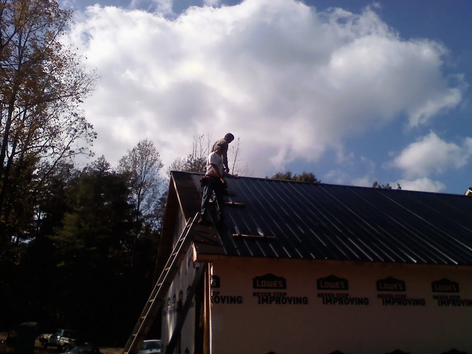 Roofer fastening dark metal panels high against a cloudy sky, from a Roof Inspection job in Bennington